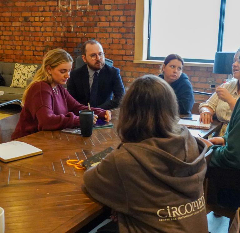 a group of 6 women and one man sit around a table on a training session