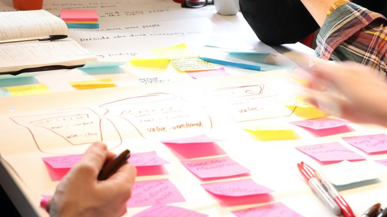 Table covered in white paper covered with pink, yellow and blue post-its and lots of colourful unreadable words.