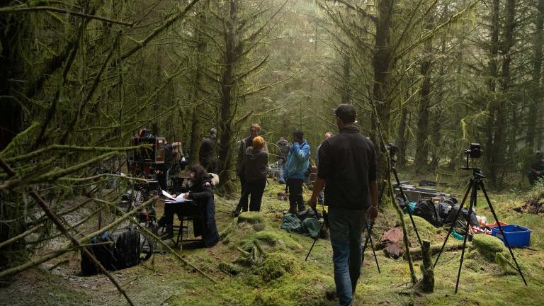 Group of people gathering in forest location with tall green trees and mossy green floors to film