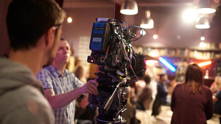 Over the shoulder shot of a person operating a big TV camera in a studio