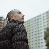 A person wearing a black jacket stares up to the sky.